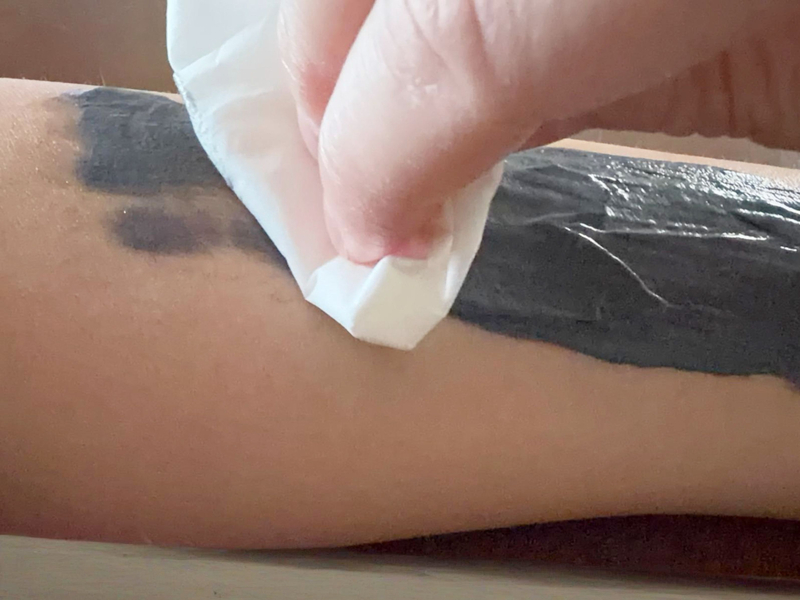 5分経過後、腕に塗った「つるるんたん」の黒いクリームをティッシュで優しく拭き取っている様子