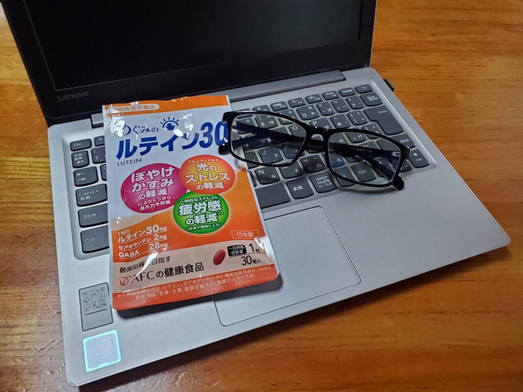 パソコンのキーボードとメガネの横に置かれためぐみのルテイン30のパッケージ袋